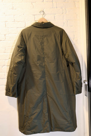 Green coat hanging on a hook against a white brick wall.