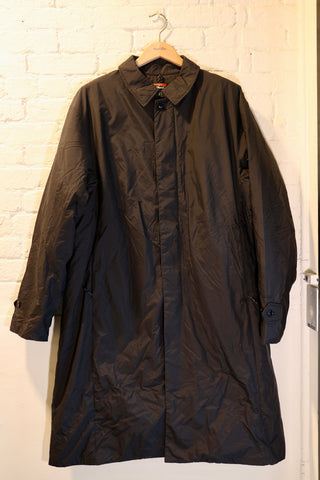 Black coat hanging on a hanger against a white brick wall.