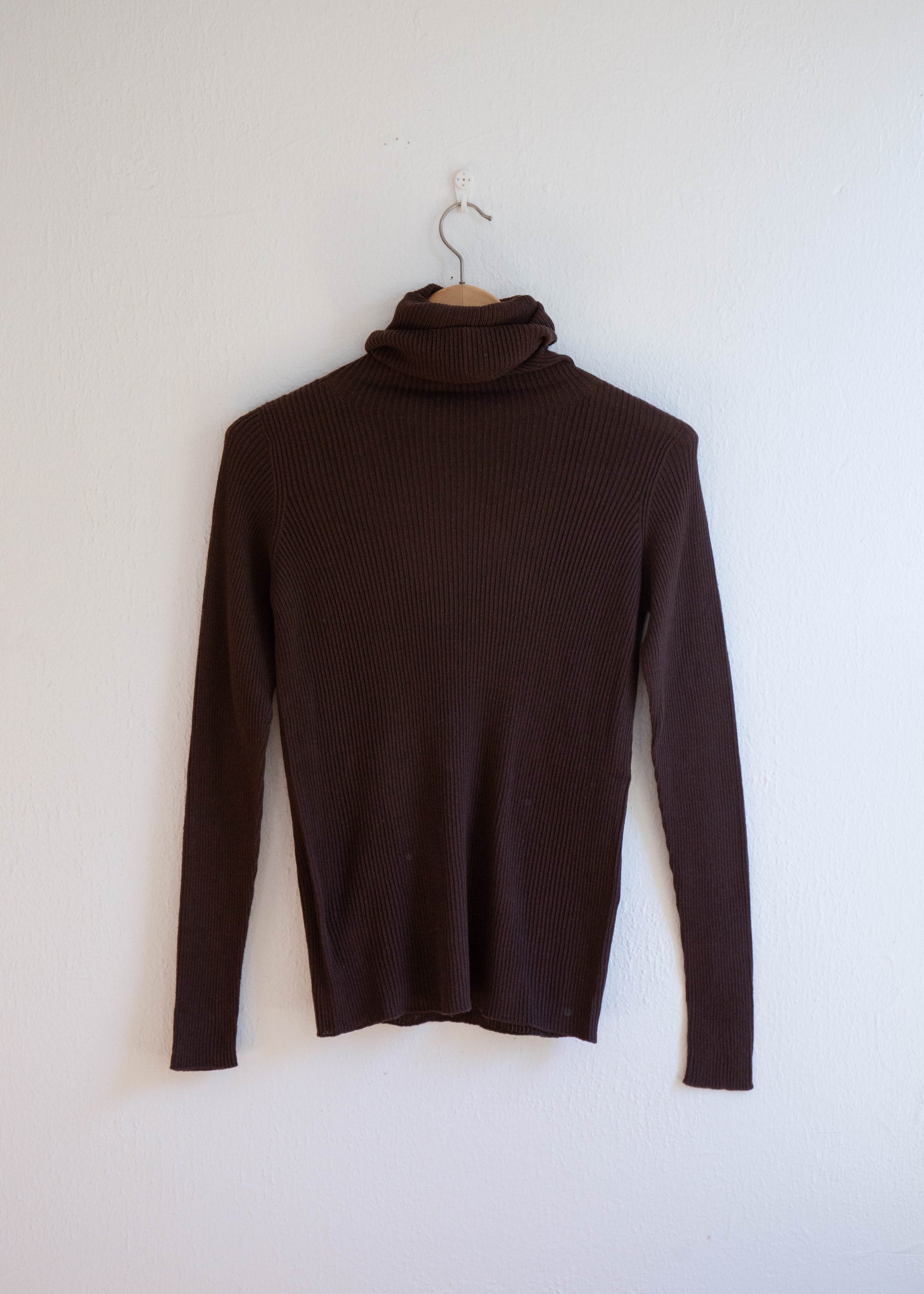 Whole garment rib turtleneck pullover color brown hanging on white wall