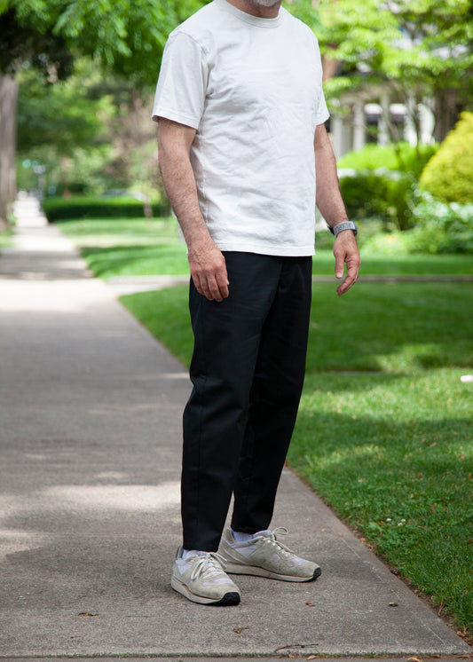 Model outdoors wearing white t-shirt, black lightweight danver pants and white/grey sneakers front