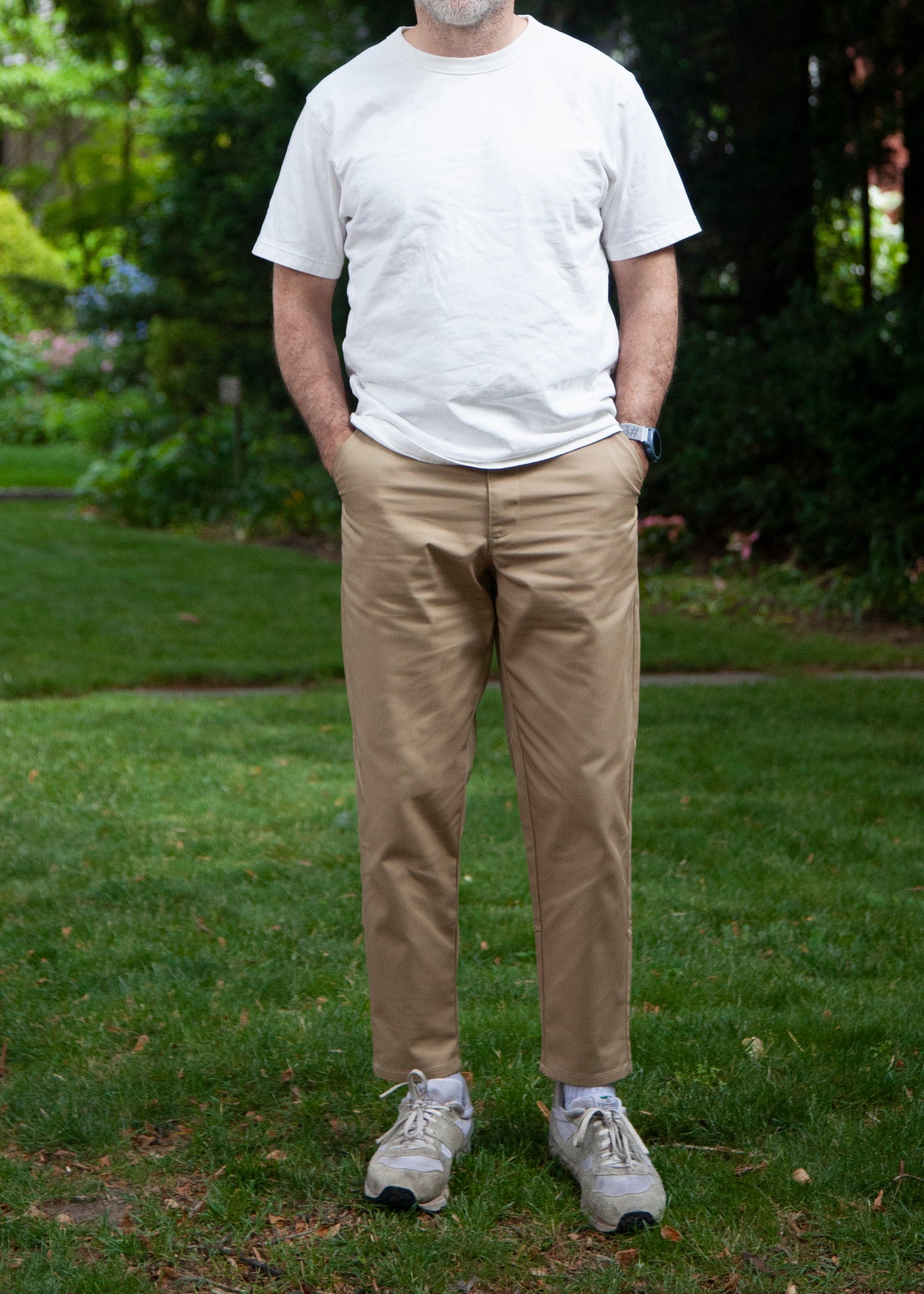 Model standing on grass wearing white t-shirt, khaki lightweight danver pants and white/grey sneakers. Front