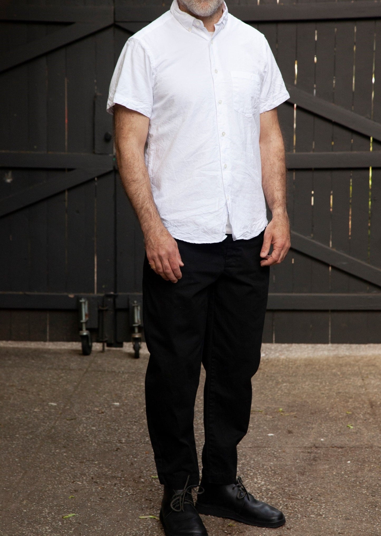 Model front standing up wearing short sleeve single needle shirt in white crinkle cotton, black llightweight danver pants and black shoes