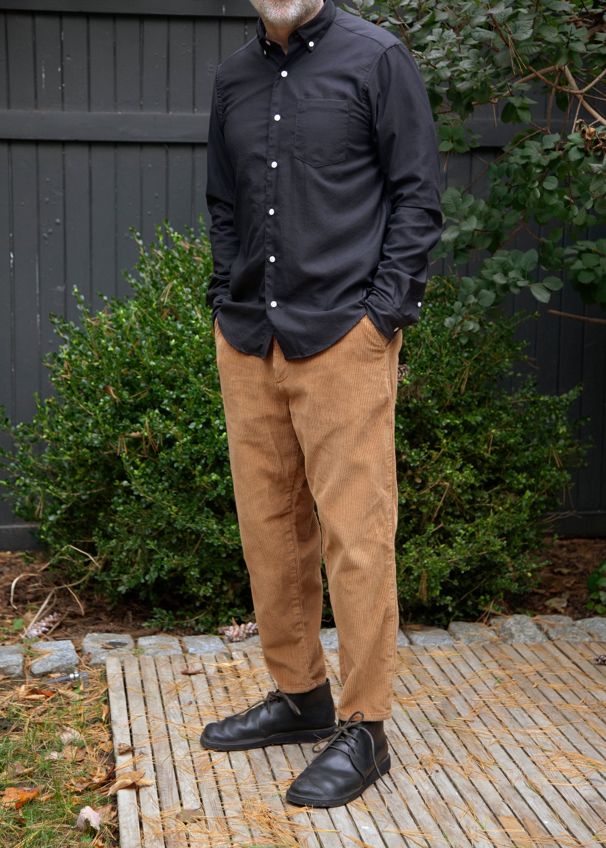 Model standing wearing single needle shirt in black nylon and brown corduroy pants