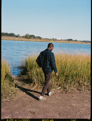 Back shot of model wearing double pocket shirt jacket in blacwatch wool and danver pants in color chocolate