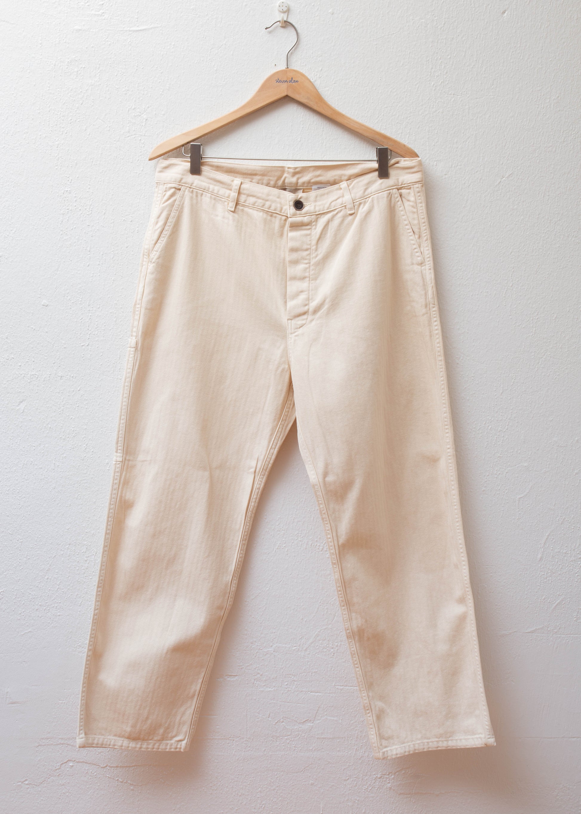 Herringbone Over Dye Pants color Ivory hanging on white wall 