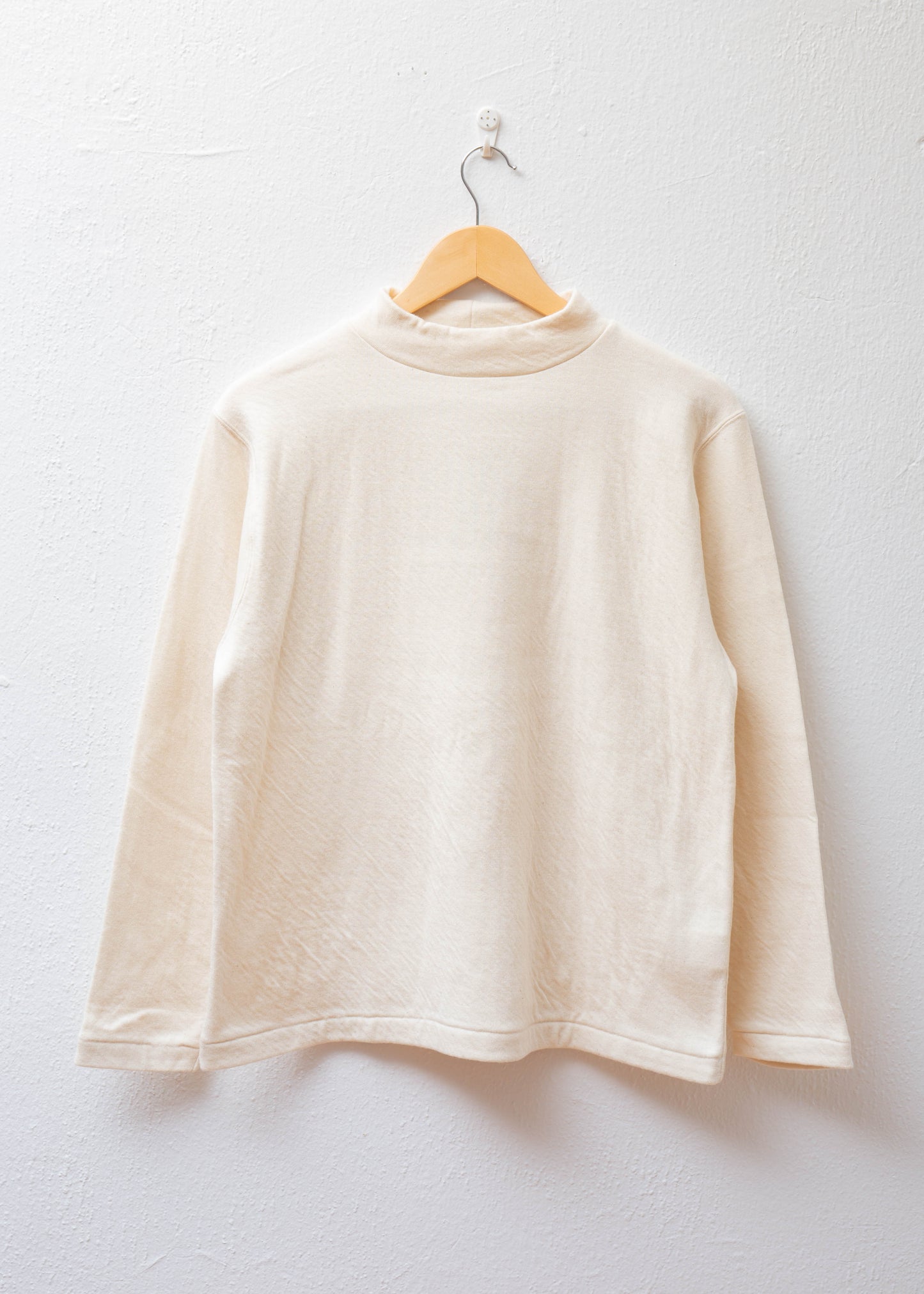 Mock Neck Pullover in color natural hanging on white wall