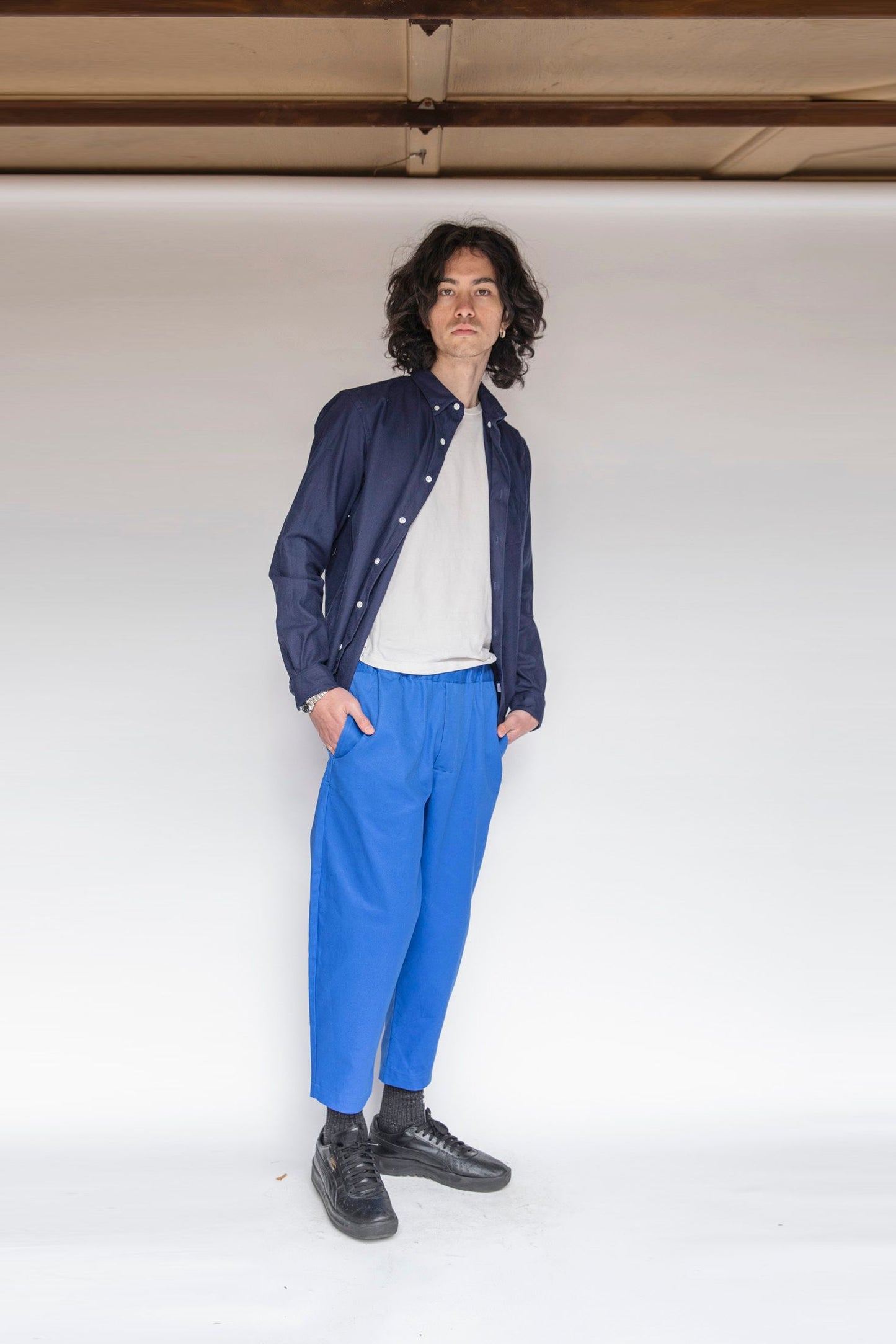 Model standing up wearing single needle shirt deep navy canvas, white t-shirt, marine blue gathered pants and black shoes 